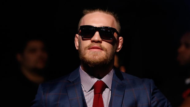 Conor McGregor head shot with blue plaid suit, red tie and sunglasses.