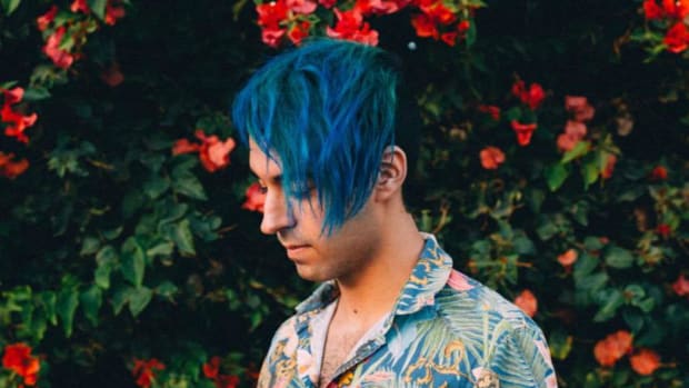 Bass music DJ/producer Luca Lush standing in front of a flowering bush.