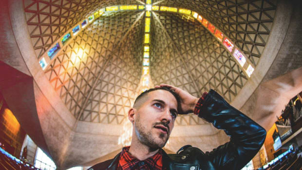 DJ/producer ANGELZ sitting in a cathedral or church with stained glass windows.