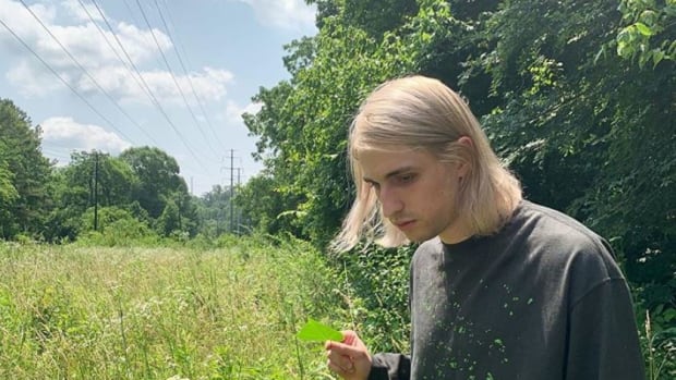 Porter Robinson with blonde hair standing in a grassy meadow.