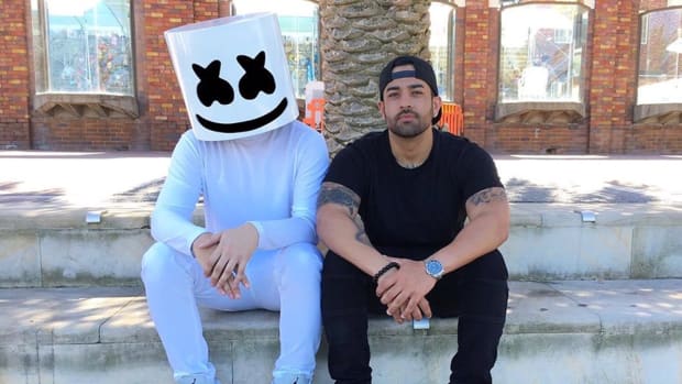 Anonymous DJ/producer Marshmello and his manager, Moe Shalizi, sitting on steps by a palm tree.