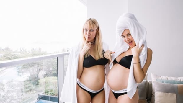 A photo of twin DJ duo Olivia and Miriam Nervo, known professionally as NERVO, with matching pregnancy baby bumps.