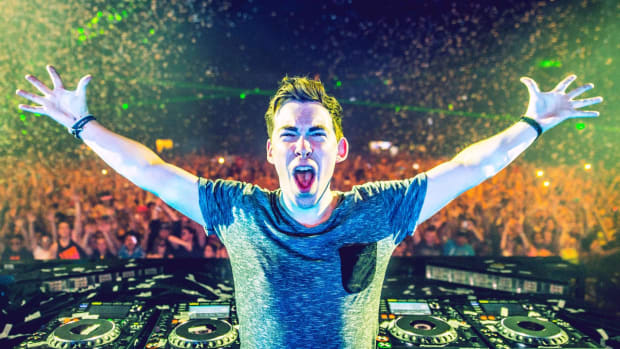 Hardwell with arms stretched out behind the DJ decks during a performance as confetti falls over the crowd in the background.