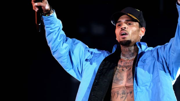 A photo of singer/songwriter/dancer Chris Brown wearing a bright blue jacket and holding a microphone during a performance.