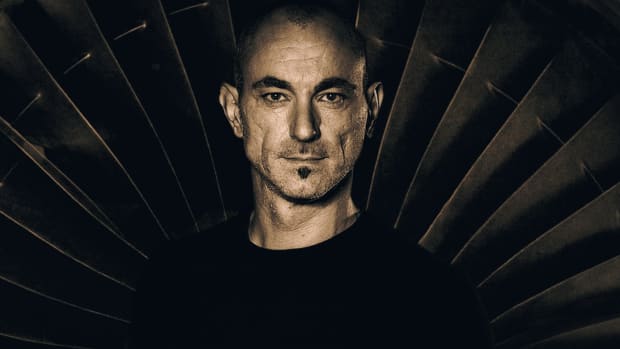 A sepia tone press photo of DJ/producer Robert Miles standing in front of a fan or turbine.