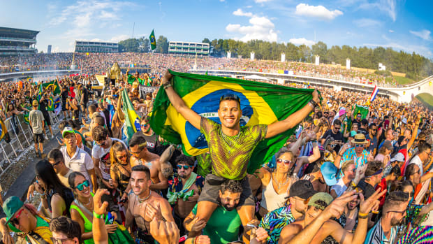 Tomorrowland Brazil Returning to São Paulo in 2023 with man on top of shoulders holding Brazil flag and dancing in a crowd of people.