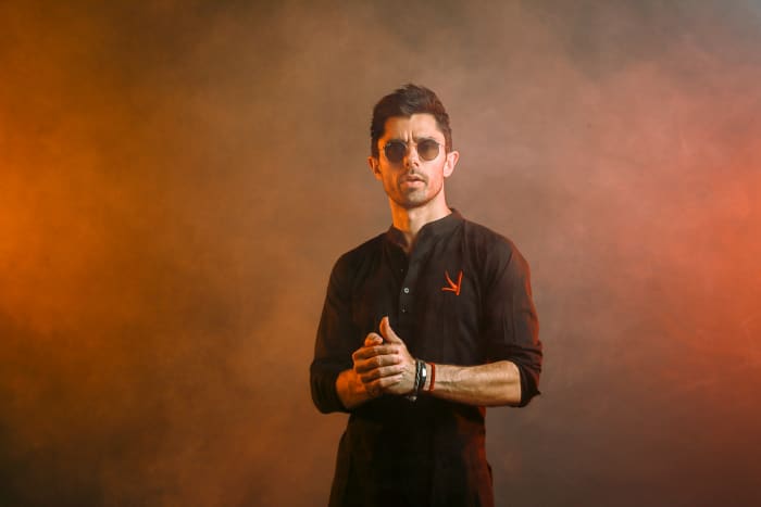 DJ/producer KSHMR over a reddish background.