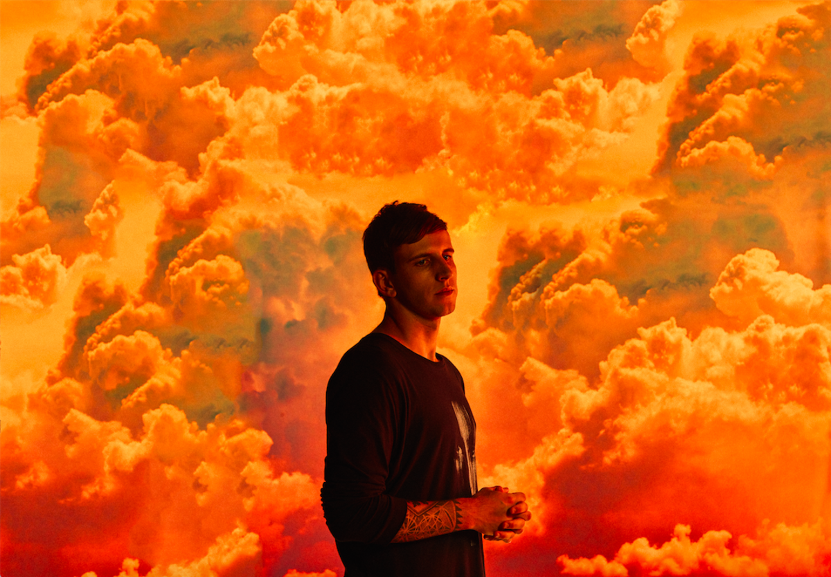 Denver EDM DJ/producer Illenium (real name Nicholas D. Miller) standing in front of orange clouds.