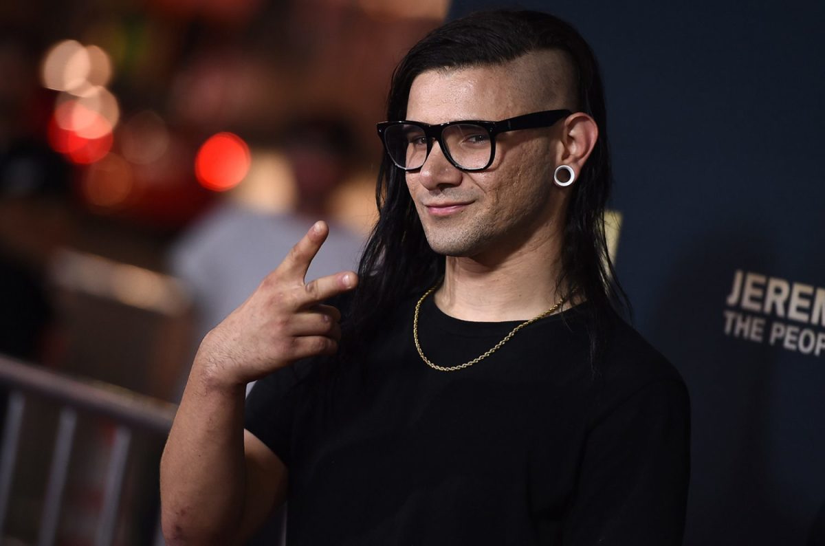 EDM DJ/producer Skrillex flashing a peace sign at a red carpet event.